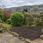 A cleared Baildon garden bed prepared for planting beside retained shrubs and a stone wall.