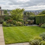 A cared-for Cottingley garden with lawn, planted borders, hedge and stone path.