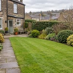 A maintained Heaton garden with a lawn, flower beds, trimmed shrubs and a stone path.
