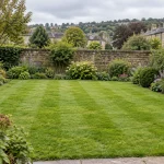 A neatly mown lawn with flower borders and a stone garden wall in Saltaire.